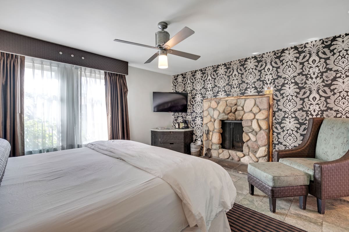 A hotel room with a large bed, a television, a fireplace, and a ceiling fan.