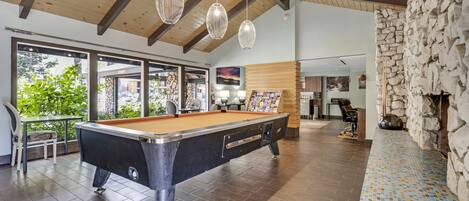 Une table de billard dans une pièce bien éclairée, avec des poutres en bois et des murs en pierre.