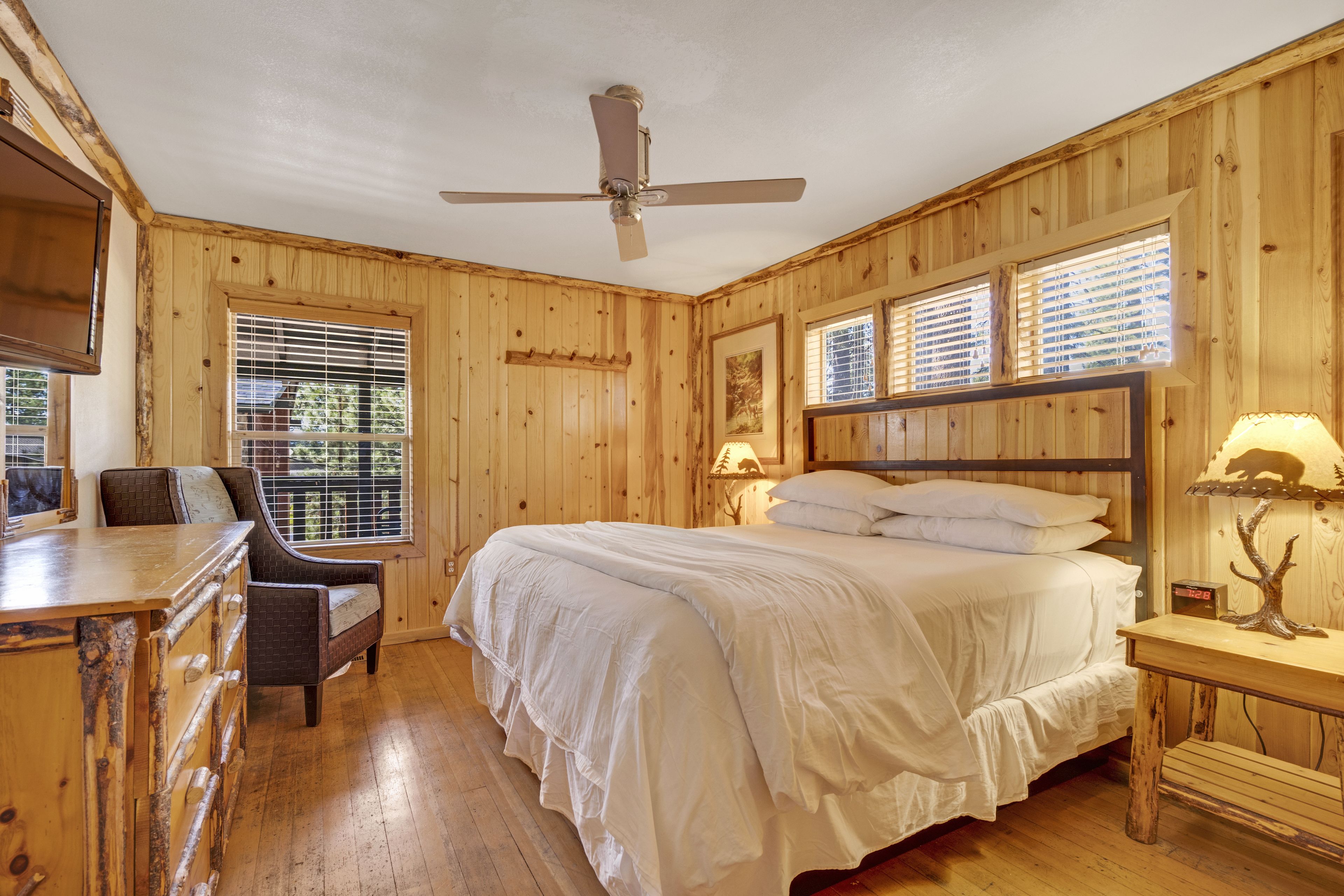 A wooden-paneled room with a bed, a desk, a chair, and a ceiling fan.