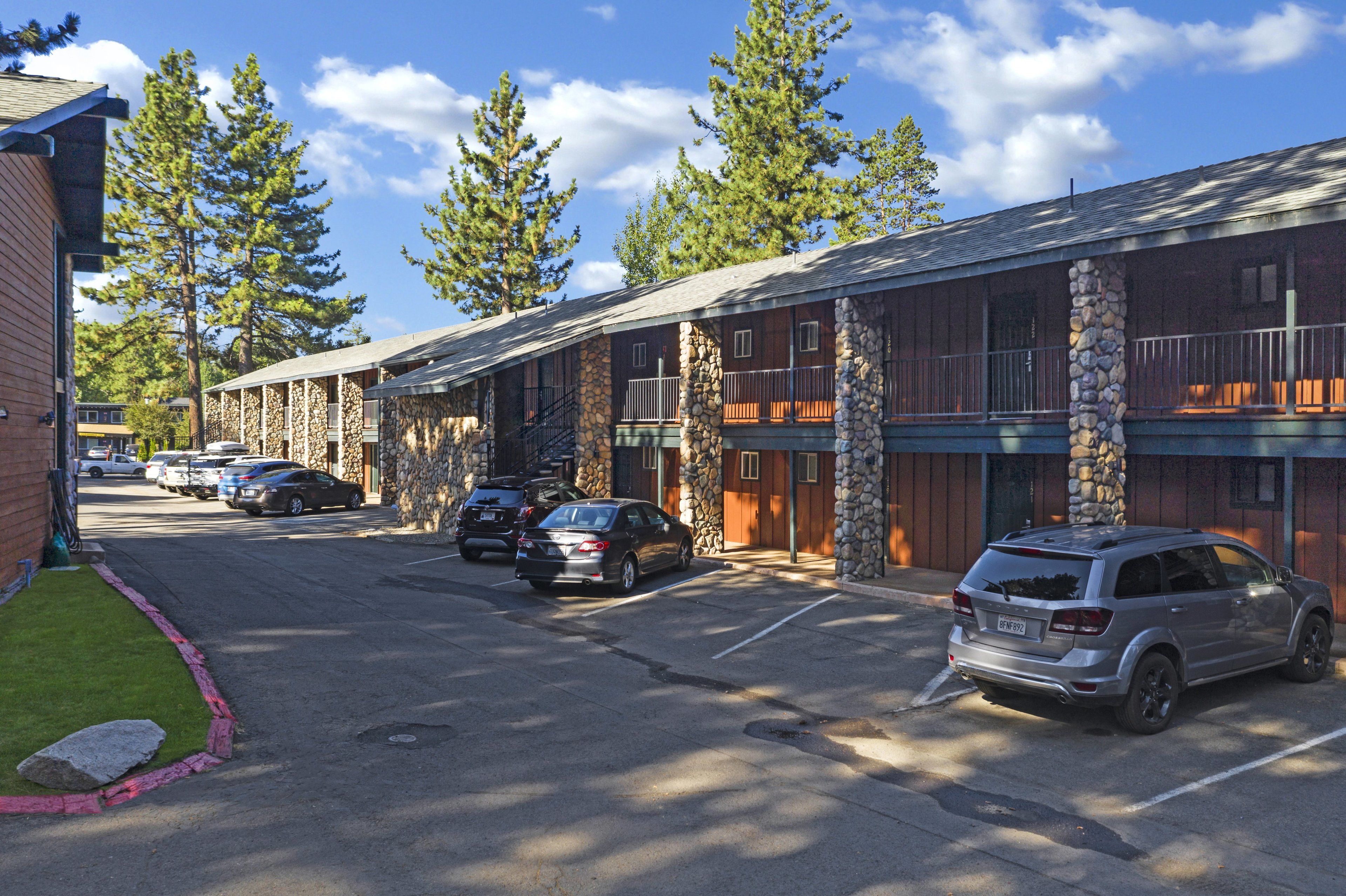 Un motel con paredes exteriores de piedra, varias habitaciones y un estacionamiento con varios automóviles.