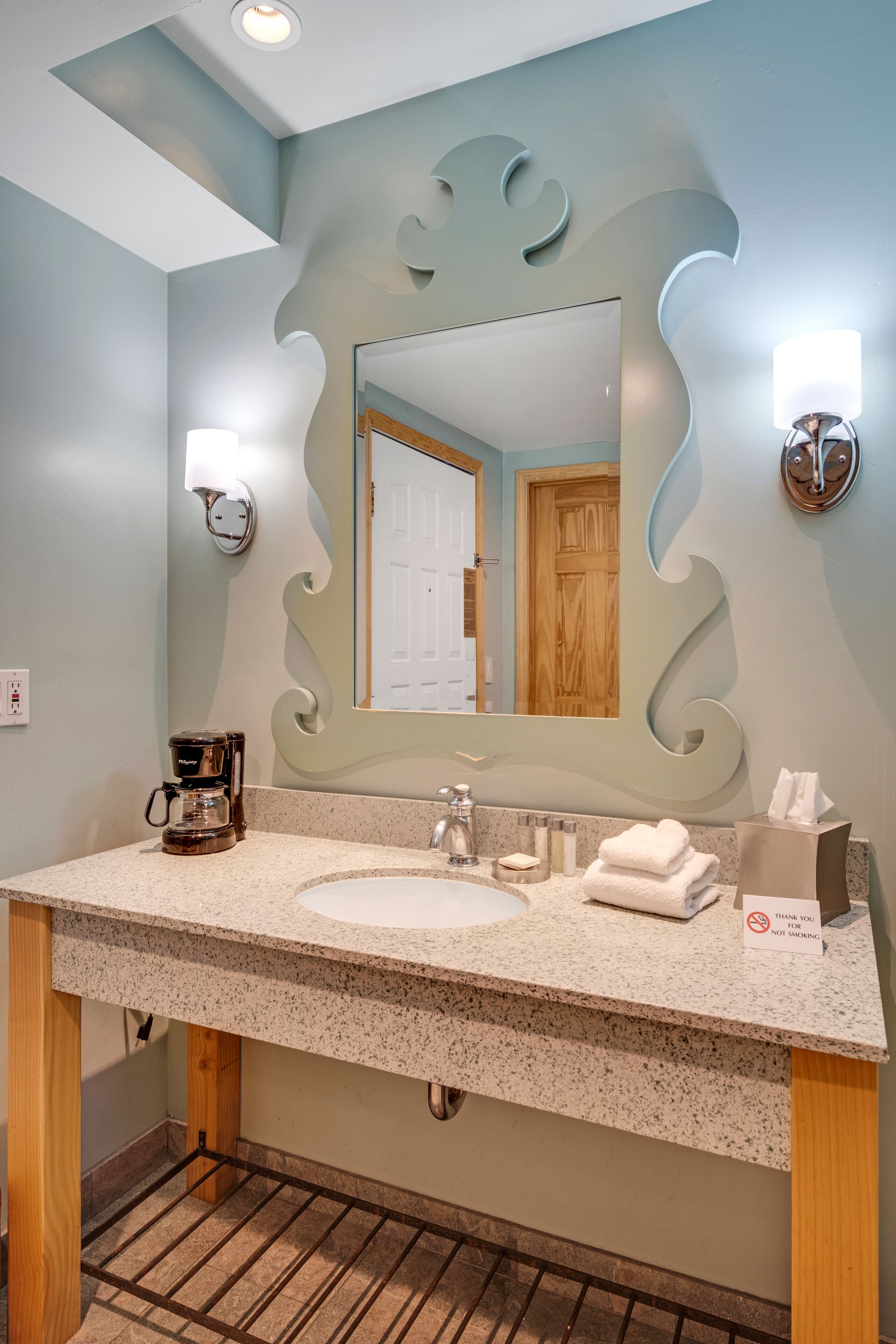 A bathroom with a large mirror, a coffee maker, and a towel dispenser.