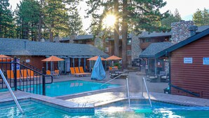 A pool area with lounge chairs and umbrellas, a stone building, and a sign indicating spa capacity.