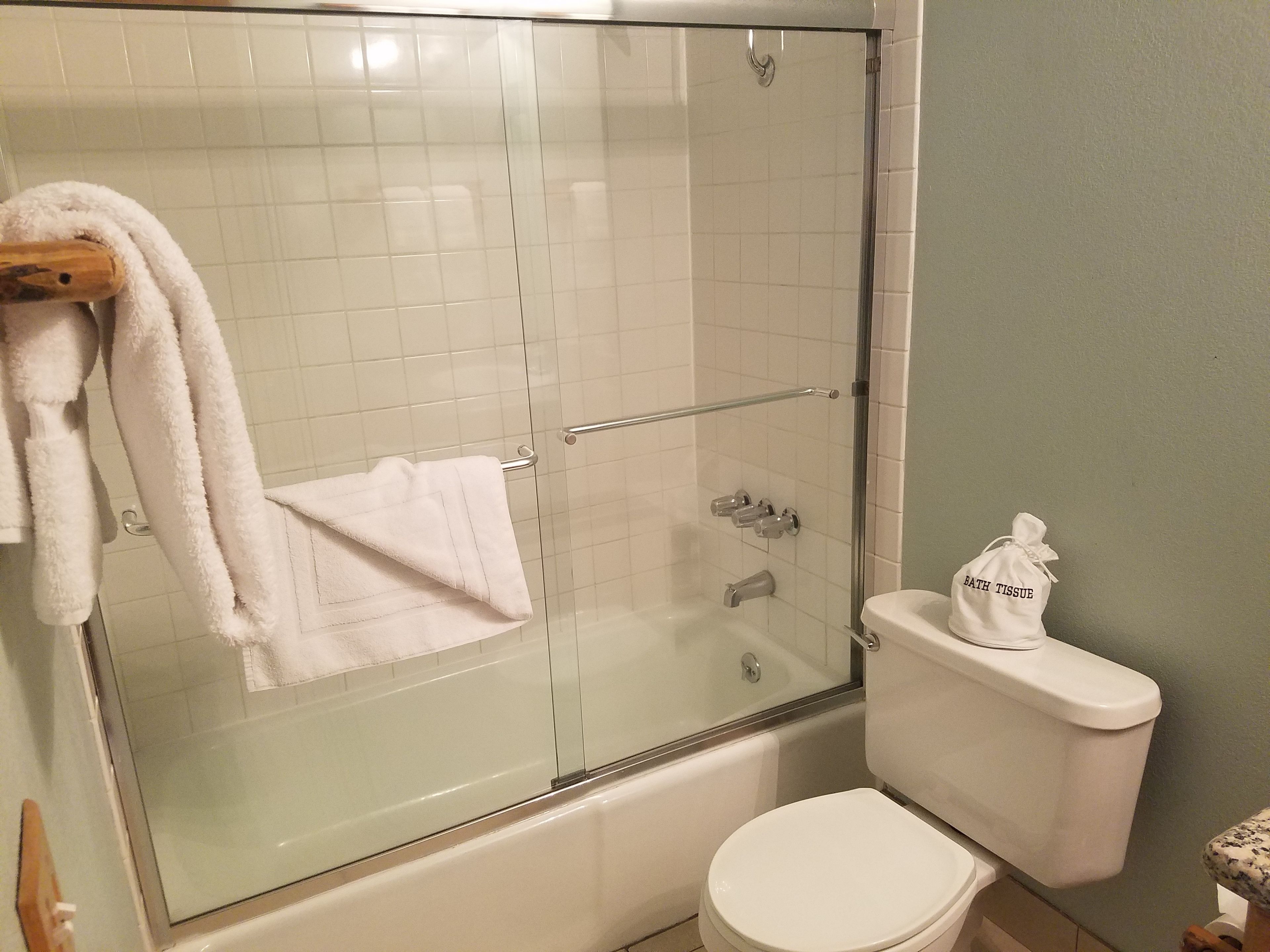 Un baño con ducha de vidrio, un inodoro blanco y una bolsa de papel higiénico sobre el inodoro.