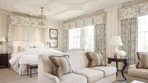 Une chambre spacieuse avec un grand lit, un canapé, deux fauteuils, une table basse en verre et une table de chevet avec des lampes.
