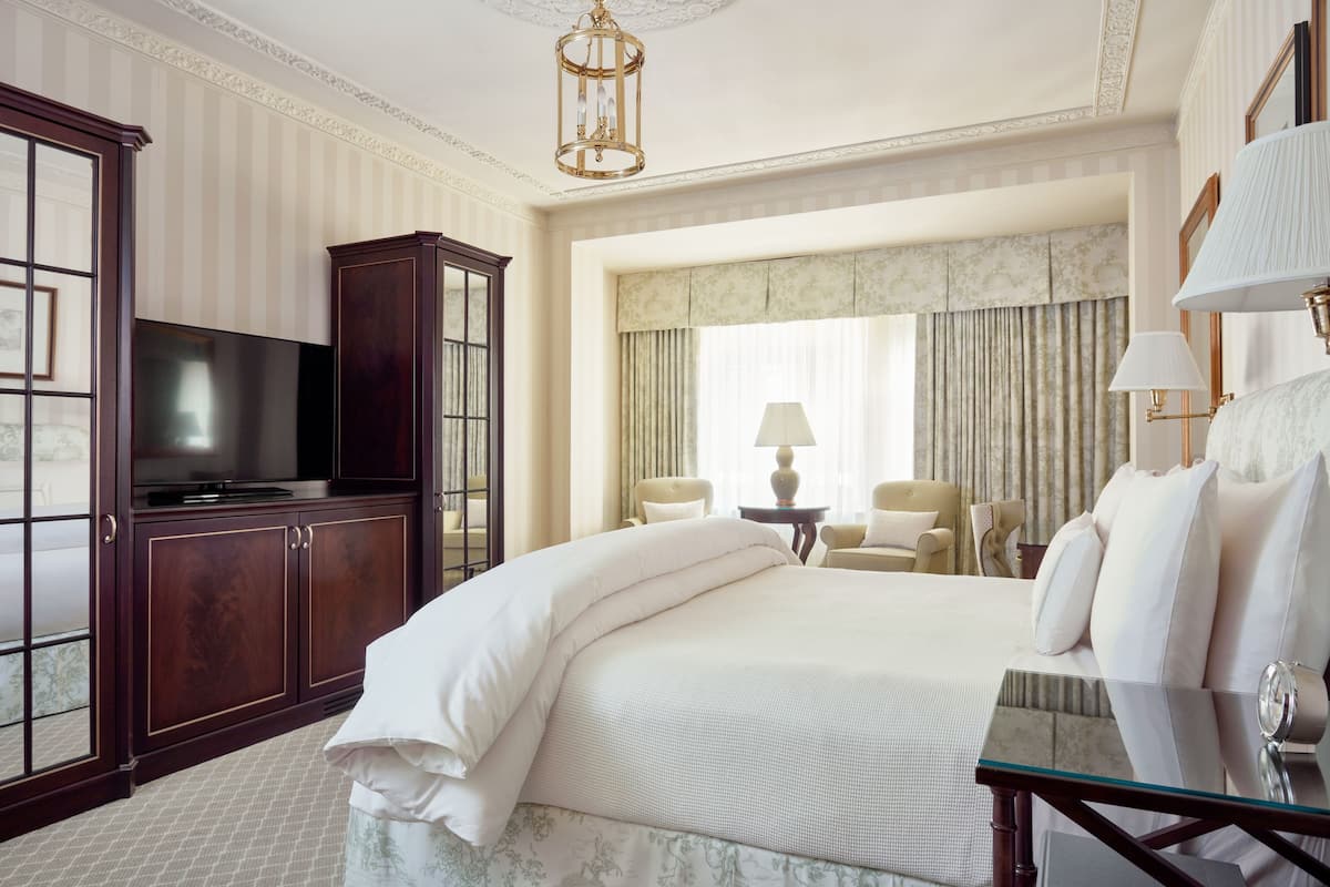 Quarto de hotel com uma cama grande, televisão, escrivaninha com abajur e uma cadeira.