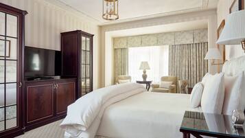 A hotel room with a large bed, a television, a desk with a lamp, and a chair.