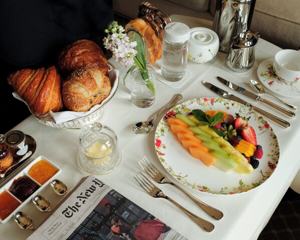 A breakfast table with croissants, a fruit plate, a newspaper, and various condiments.