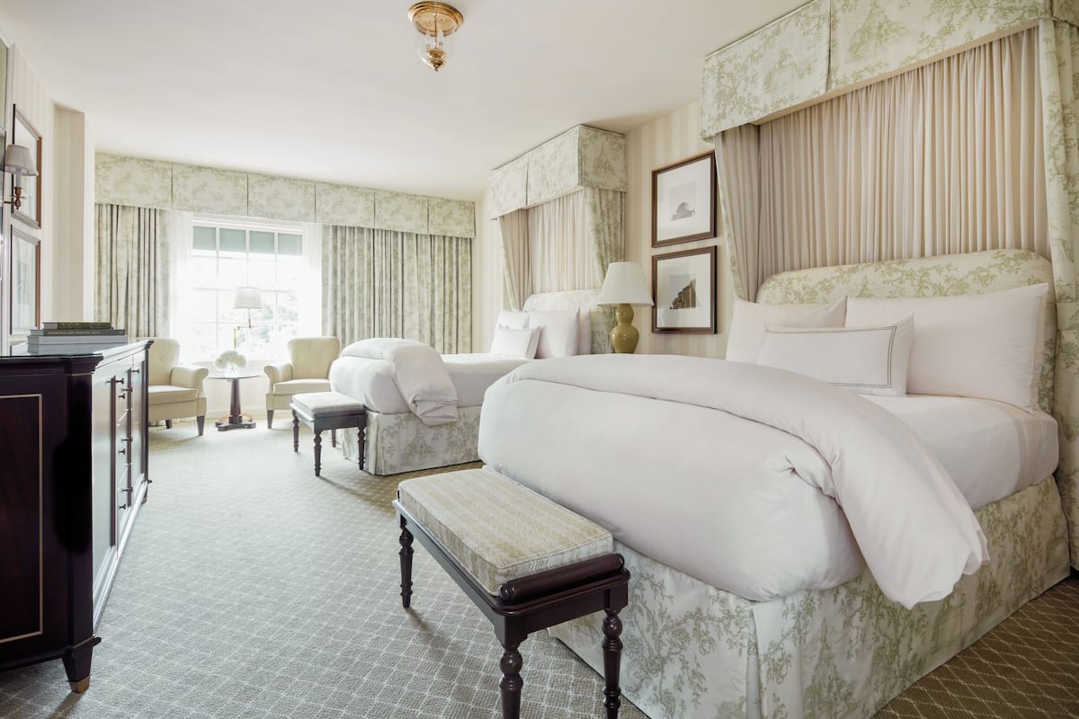 Quarto de hotel com uma cama grande, duas poltronas, uma mesinha e uma cômoda.