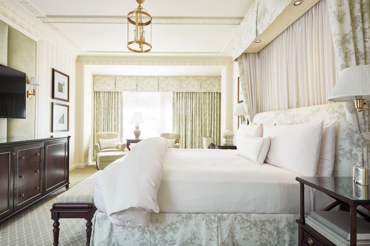 Quarto de hotel com uma cama grande, televisão, escrivaninha e uma cadeira.