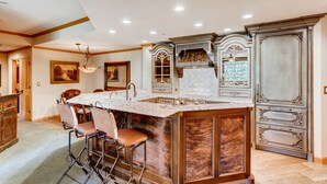A spacious kitchen with a marble island, bar stools, and a large window.