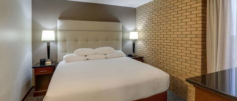 A hotel room with a large bed, two bedside tables with lamps, a brick accent wall, and a view of the outdoors.