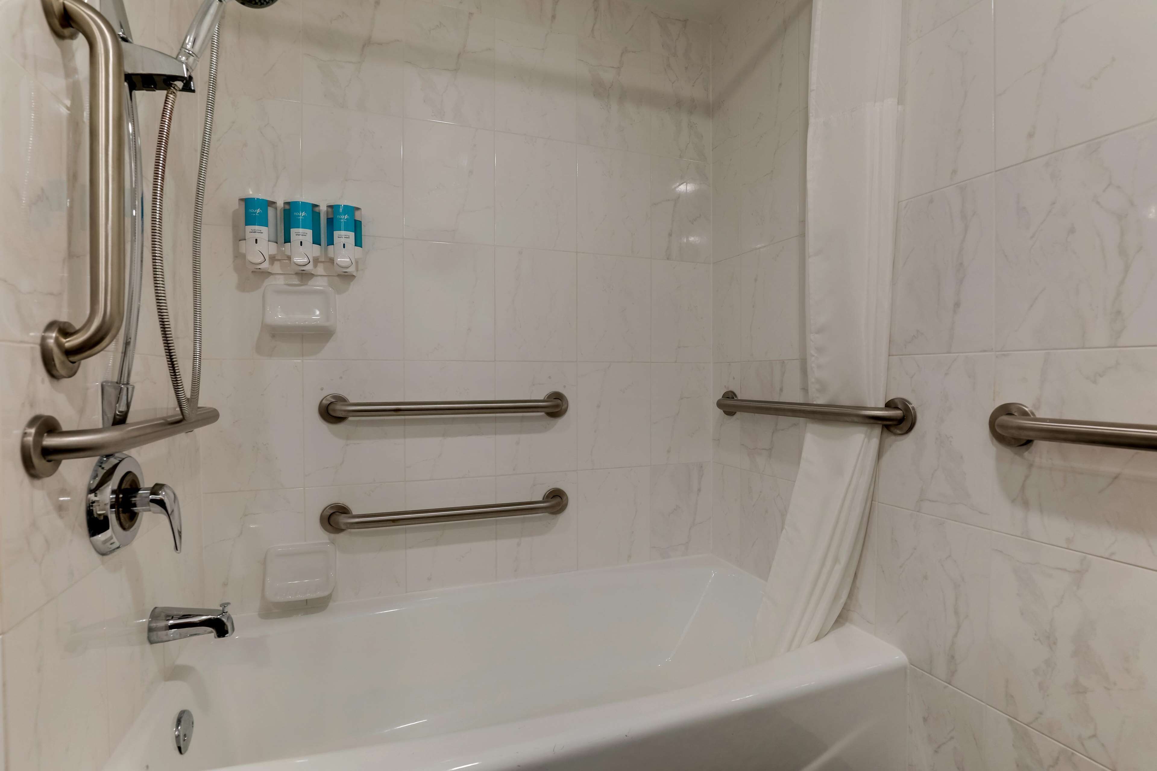 Baño con bañera, barras de apoyo, ducha y dispensadores de jabón.