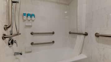 Baño con bañera, barras de apoyo, ducha y dispensadores de jabón.