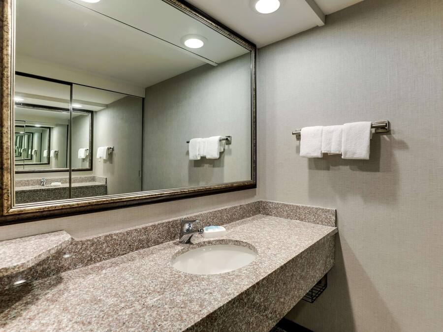 Un baño con lavamanos de encimera de granito, un espejo grande y dos barras para toallas.