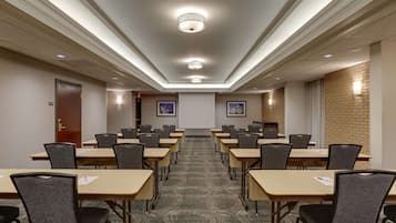 Un salón de conferencias con una larga mesa, sillas, una pantalla de proyector y piso alfombrado.