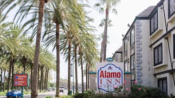 A sign for Alamo Inn & Suites with a clear view of the building's architecture and surrounding palm trees.