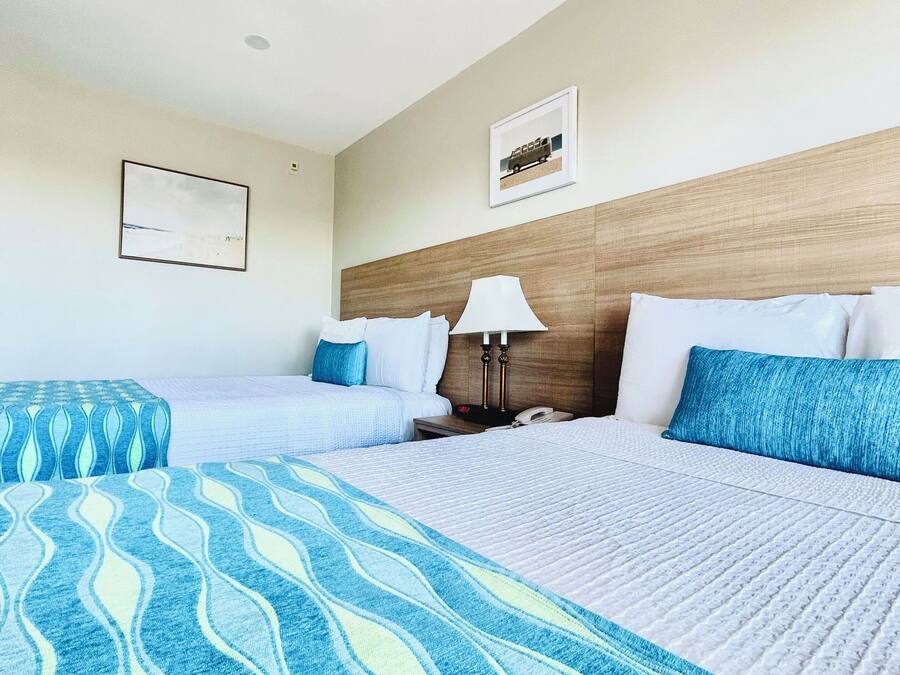 Ein Hotelzimmer mit zwei Betten, einem Holz-Kopfteil, einem Nachttisch mit Lampe und einem gerahmten Bild an der Wand.