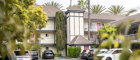 A multi-story hotel with a parking lot, palm trees, and a building with balconies.