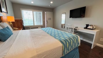 Ein Hotelzimmer mit Bett, Schreibtisch, Stuhl, Fernseher und einem Fenster mit Jalousien.