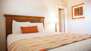 A neatly made bed with a patterned bedspread, a wooden headboard, and a single orange pillow.