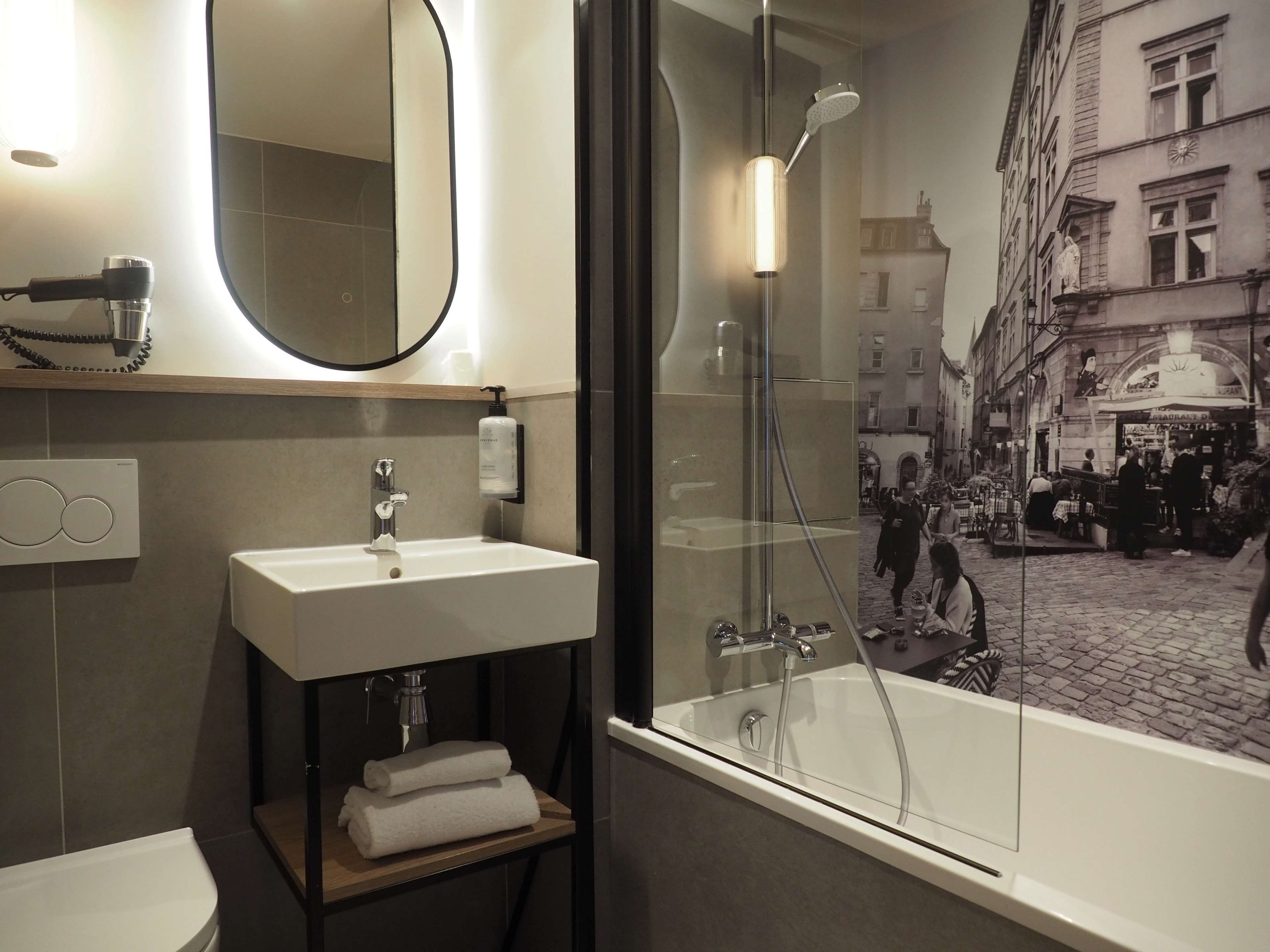 Un bagno moderno con uno specchio grande, un lavandino, una cabina doccia in vetro e vista sulla strada attraverso la porta della doccia.