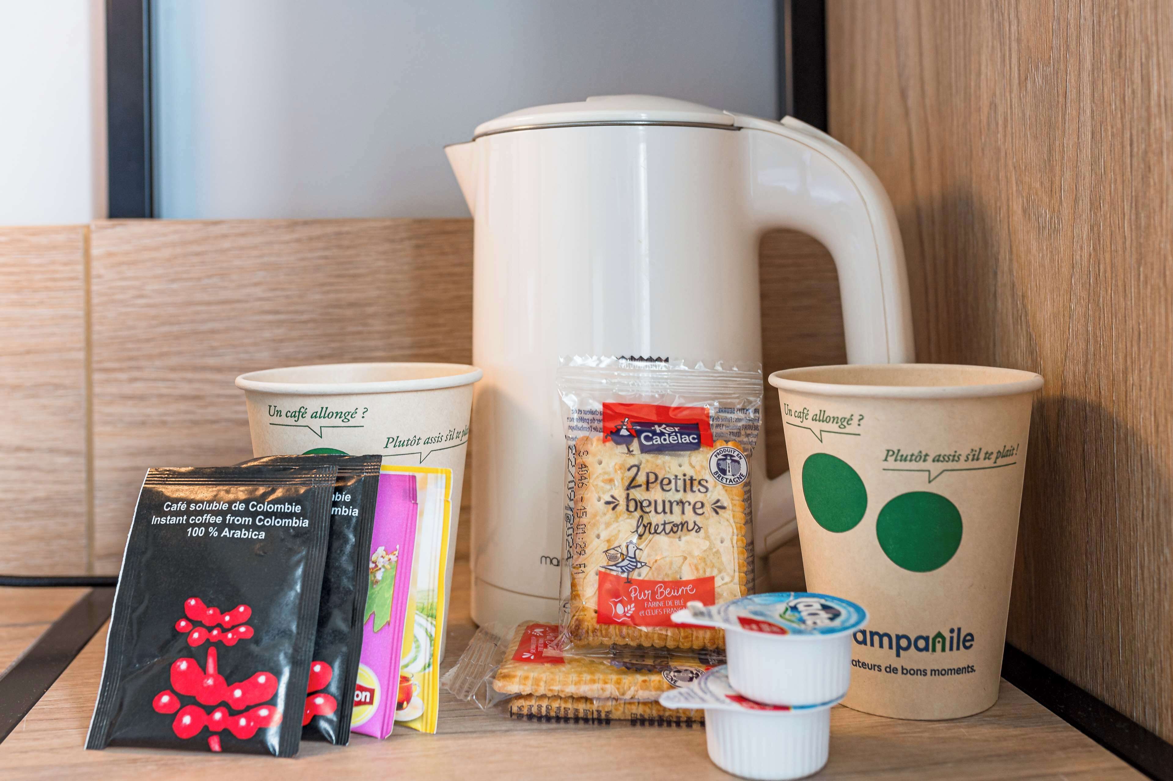 Een koffiezetapparaat, zakjes instantkoffie, een pak koekjes, een yoghurtbeker en een mok met groene cirkels.