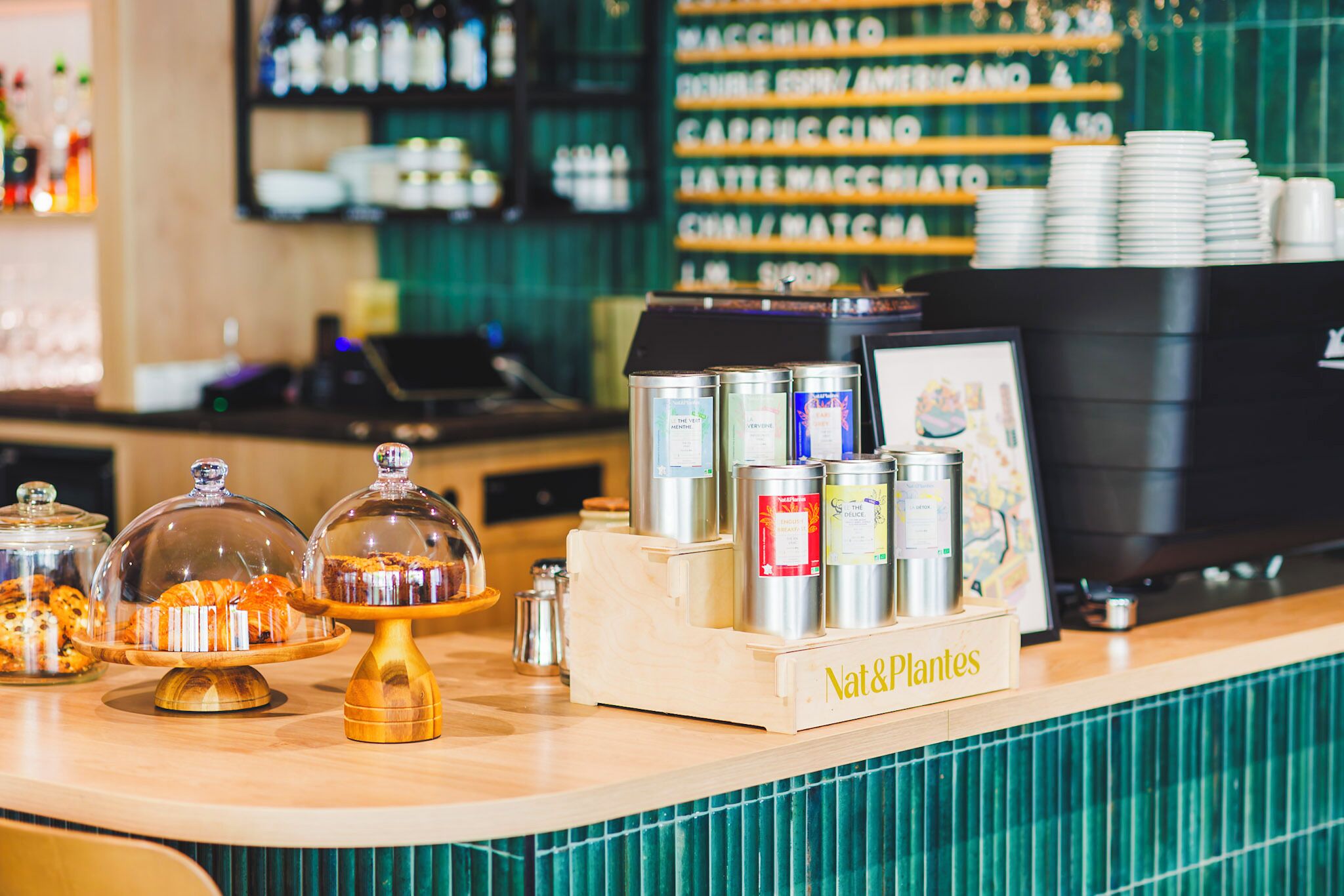 A café counter with a coffee machine, a display of canned beverages, and a sign reading 'Nat&Plantes.'