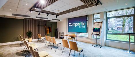 Un salón de conferencias con una pantalla grande mostrando 'Campanile Prime', una pizarra y vistas al exterior a través de amplios ventanales.