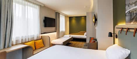 A hotel room with a large bed, a sofa, and a smaller bed. There is a TV mounted on the wall and a painting above the sofa.