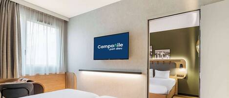 Habitación de hotel con dos camas, televisión, escritorio y ventana con cortinas.