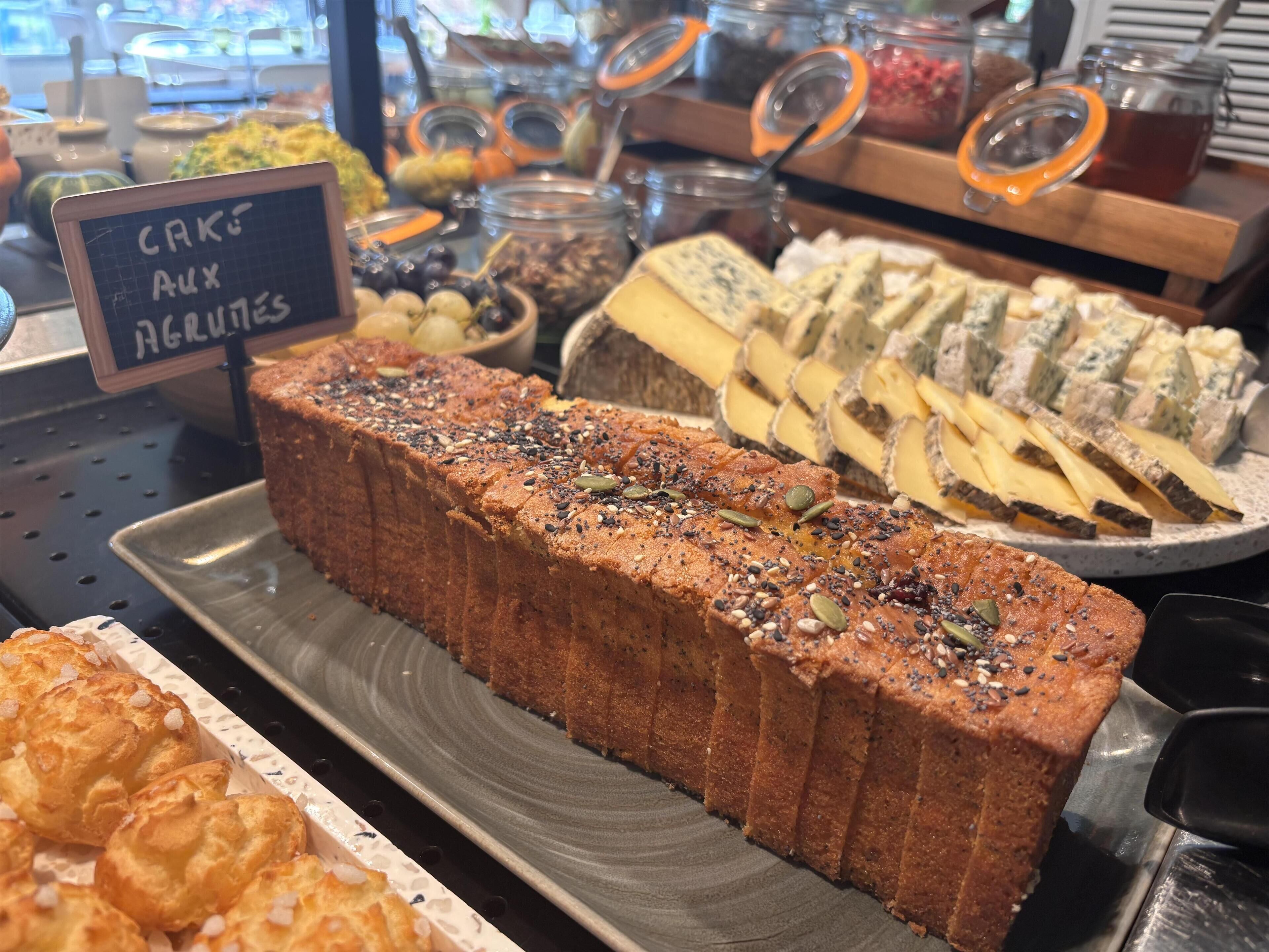 A bakery display with various baked goods including a loaf of cake, assorted cheeses, and pastries.