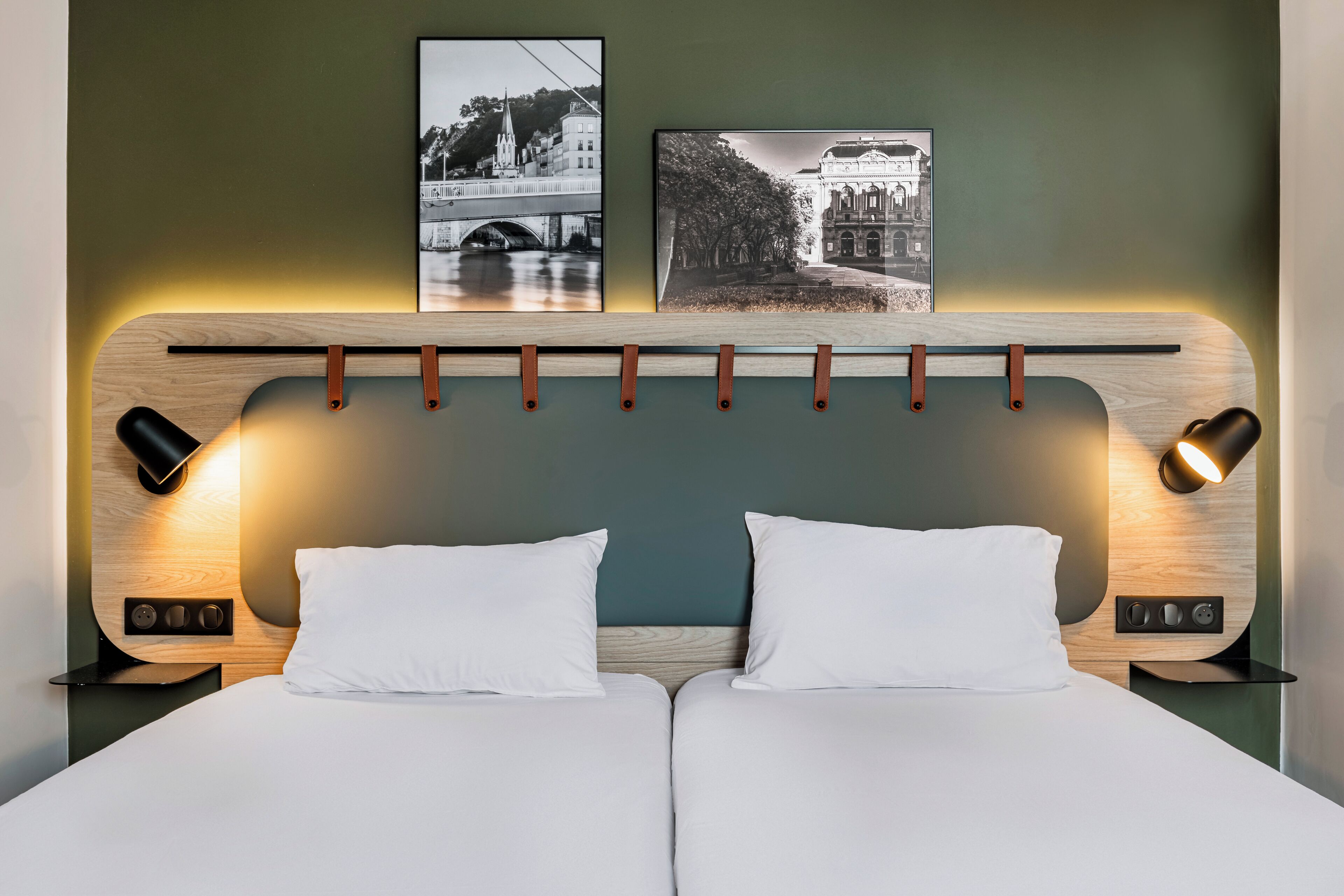 Een tweepersoonsbed met twee witte kussens, een houten hoofdbord en twee wandlampen.