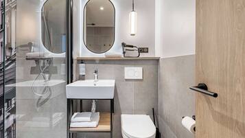Un baño moderno con cabina de ducha de vidrio, un lavamanos blanco, un inodoro y un espejo.