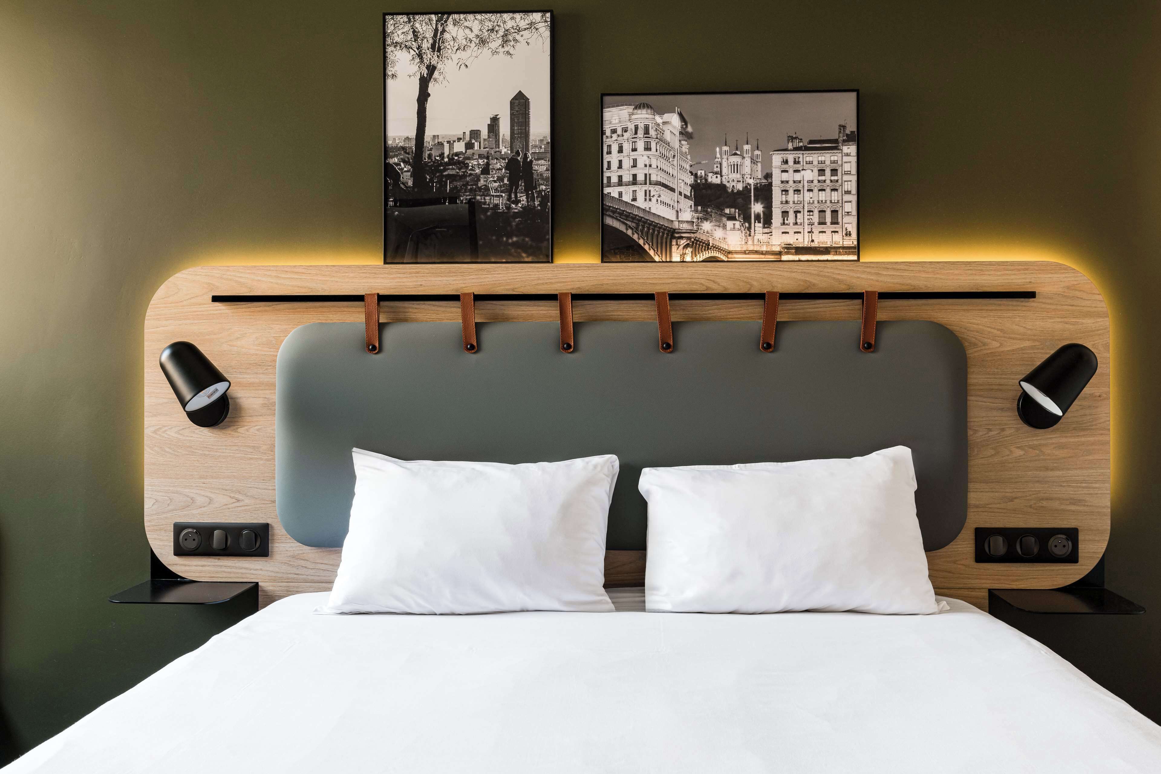 A modern hotel room with a wooden headboard, two white pillows, and two wall-mounted picture frames.