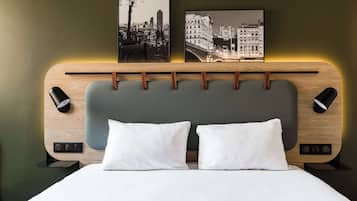 Camera d'hotel moderna con testiera in legno, due cuscini bianchi e due quadri appesi alle pareti.