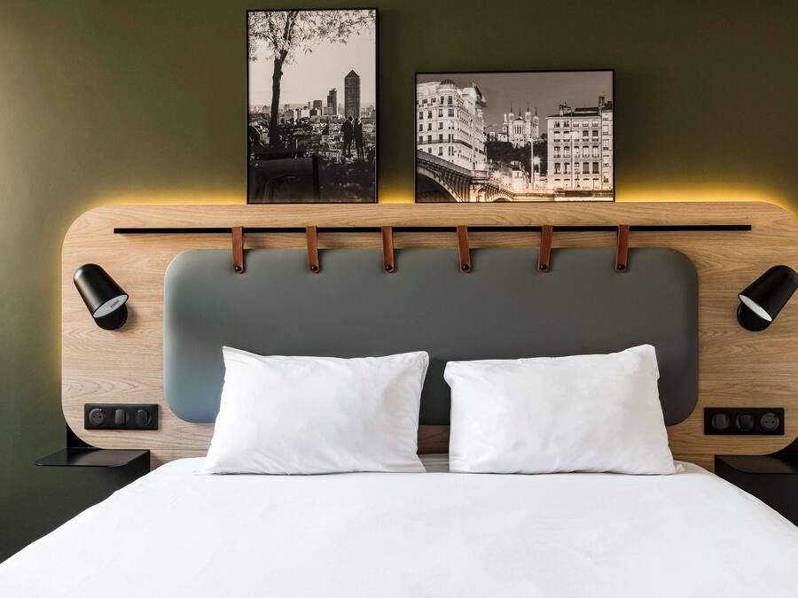 Camera d'hotel moderna con testiera in legno, due cuscini bianchi e due quadri appesi alle pareti.