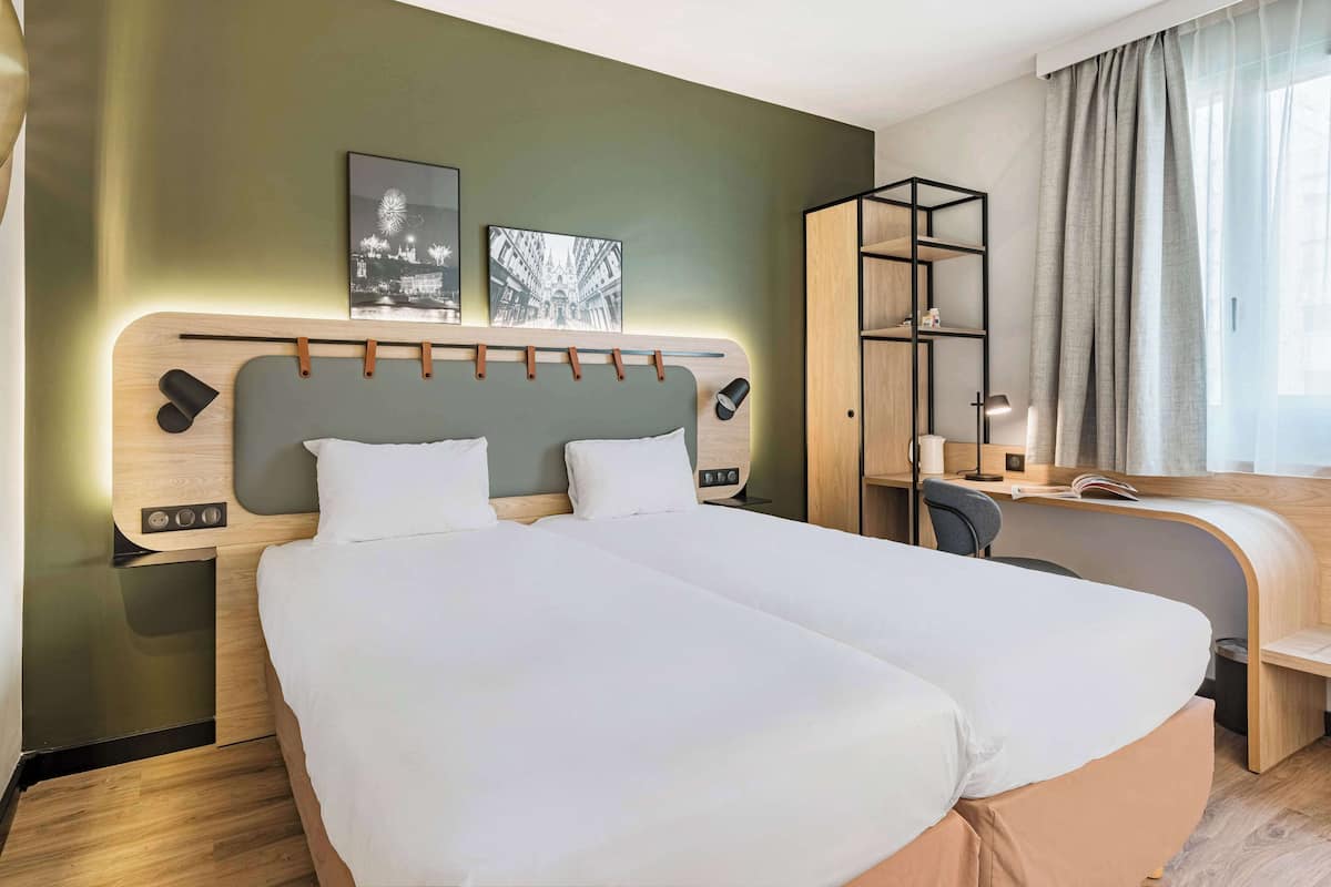 A modern hotel room with a large bed, a desk, and a wardrobe.