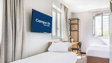 Habitación de hotel con dos camas, un escritorio con silla, un televisor montado en la pared y una estantería.