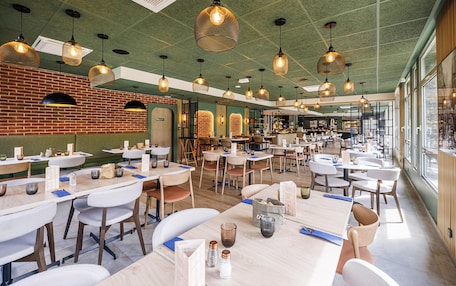 Un restaurant spacieux avec de nombreuses tables, des luminaires suspendus et de grandes fenêtres qui laissent entrer la lumière naturelle.