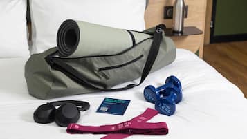 A bed with a yoga mat, dumbbells, resistance bands, headphones, and a water bottle.