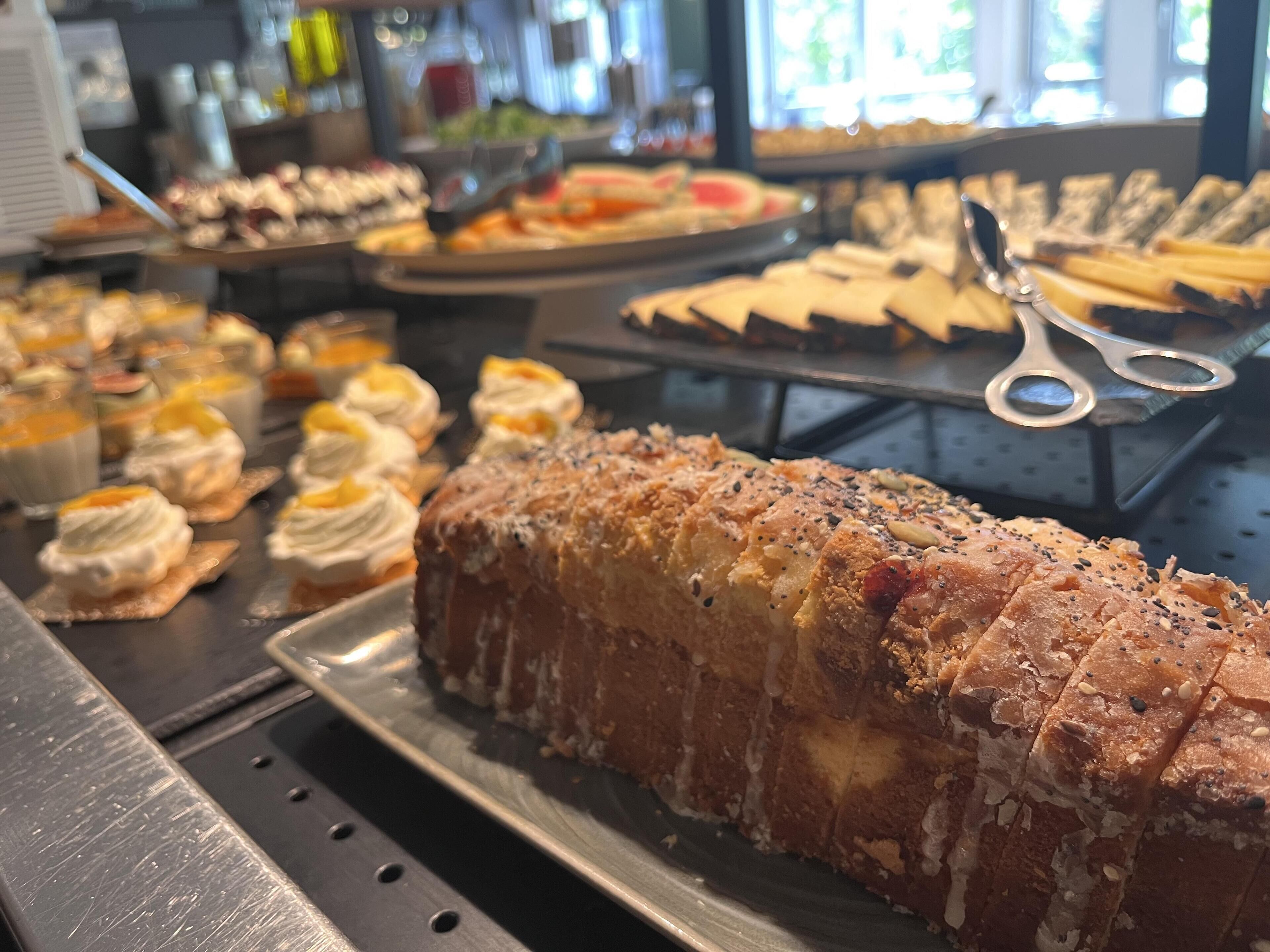 Un buffet proposant une variété de plats, notamment une grande miche de pain, des viennoiseries et des desserts.