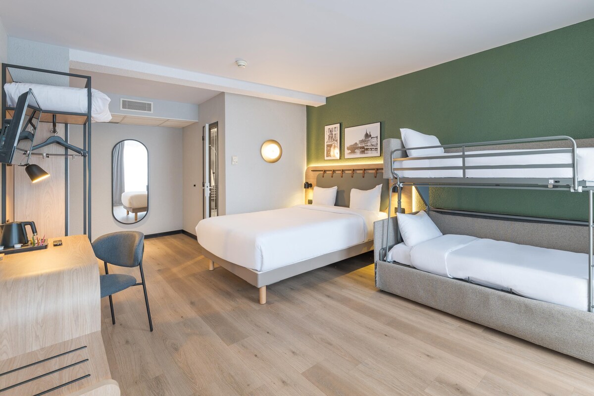 Habitación de hotel con literas, una cama individual, un escritorio con silla, un espejo y un calentador fijado a la pared.