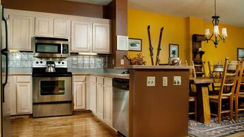 A kitchen with wooden cabinets, stainless steel appliances, and a dining area with wooden chairs and a rug.