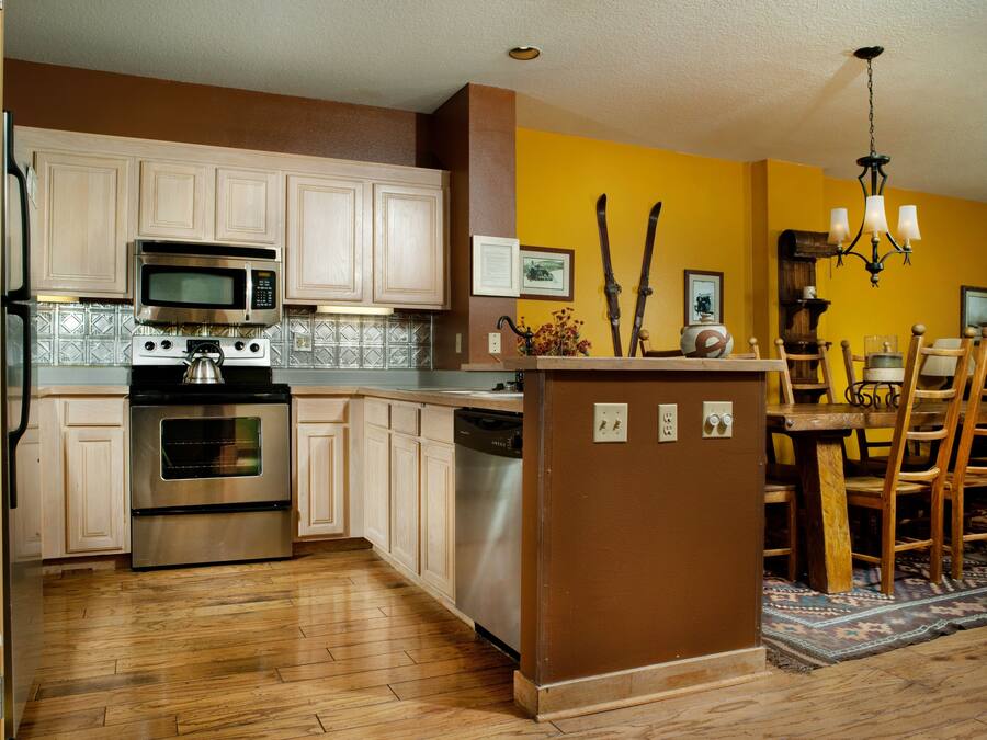 A kitchen with wooden cabinets, stainless steel appliances, and a dining area with wooden chairs and a rug.