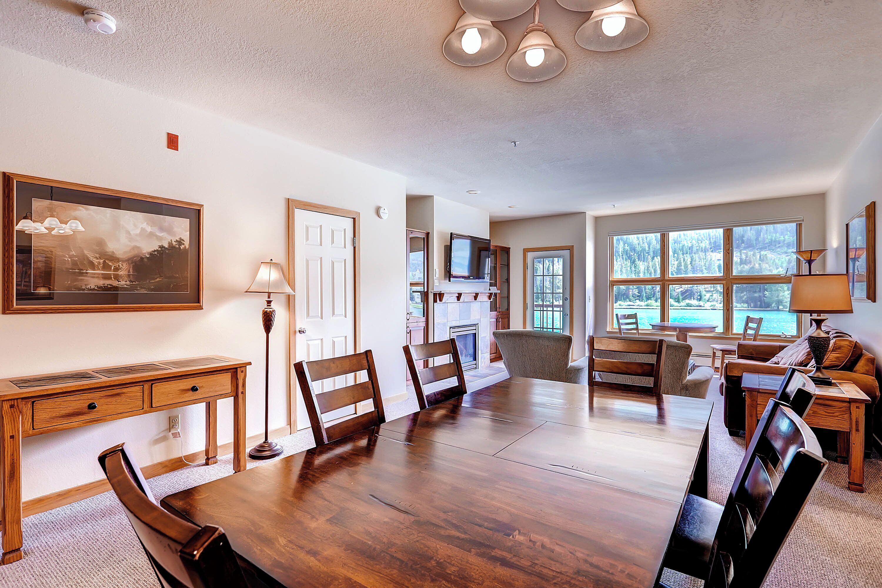 A spacious dining area with a large wooden table and chairs, a fireplace, and a view of the outdoors through large windows.
