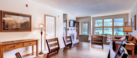 A spacious dining area with a large wooden table and chairs, a fireplace, and a view of the outdoors through large windows.