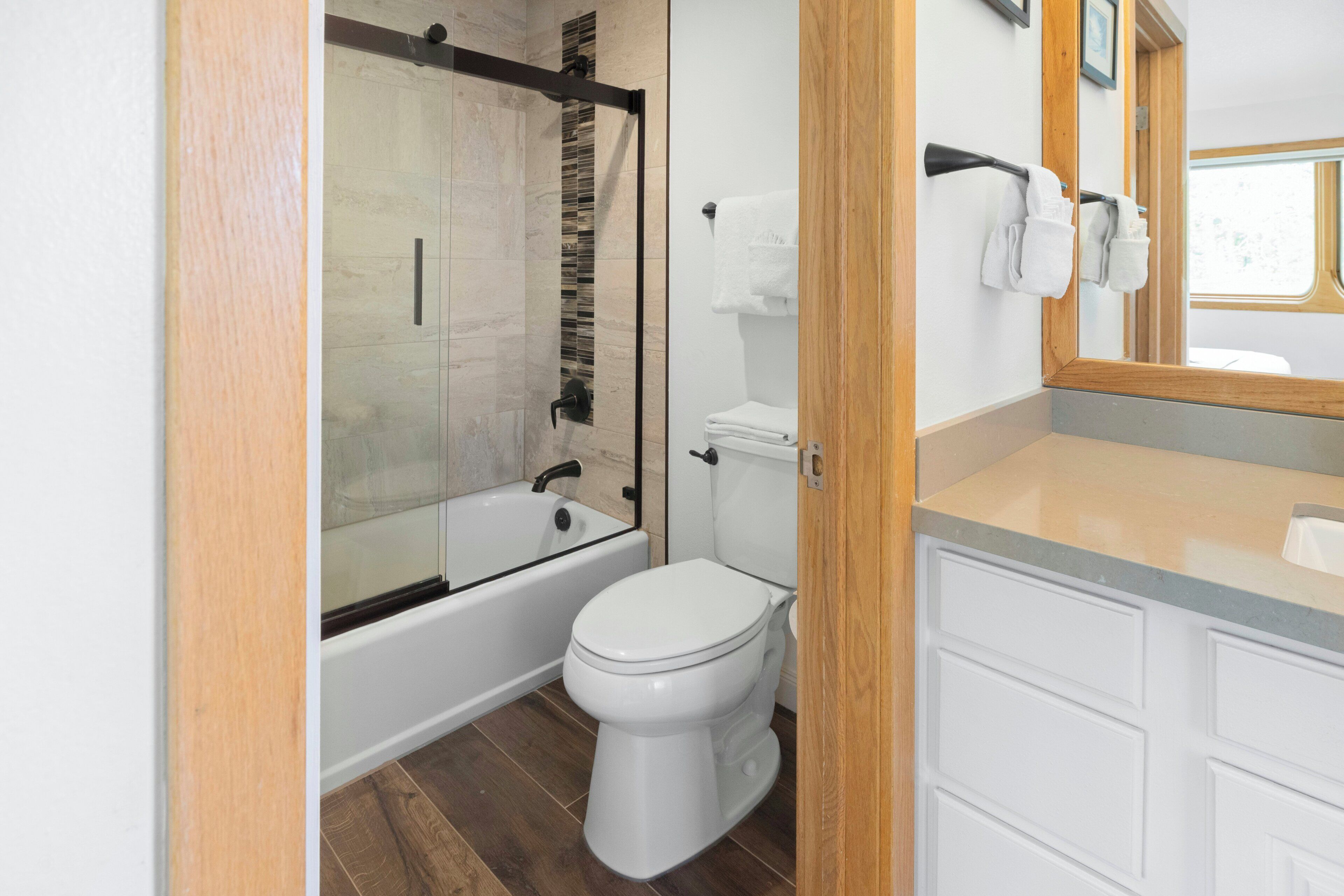 Une salle de bain moderne avec une douche à parois de verre, des toilettes blanches et un meuble-lavabo en bois avec un miroir.