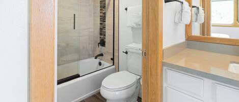 Une salle de bain moderne avec une douche à parois de verre, des toilettes blanches et un meuble-lavabo en bois avec un miroir.