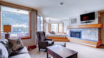 A spacious living room with a fireplace, large windows, a sofa, and a television.