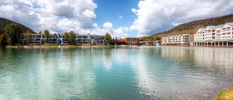 A lakeside hotel with multiple buildings, clear water, and a mountainous backdrop.
